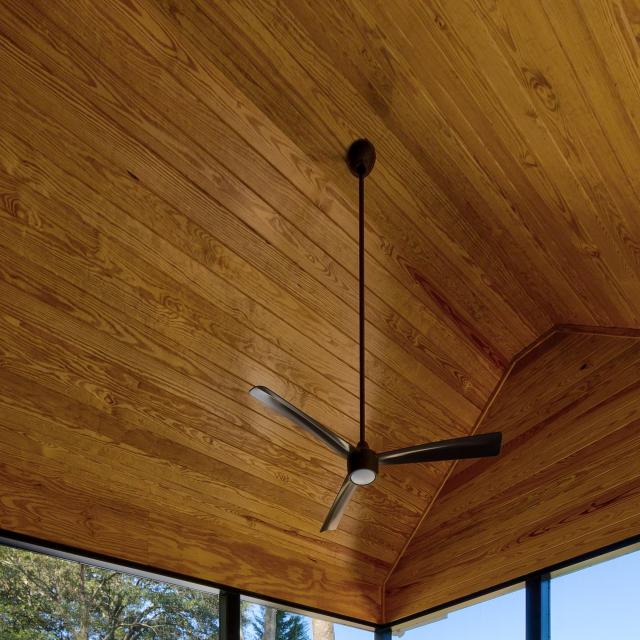 Wooden ceiling of a screened back porch with a ceiling fan. 