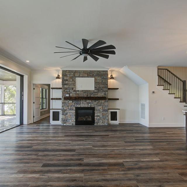 Custom Rafter B living room featuring stone fireplace and large open sliding glass doors in a lakeside home