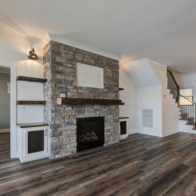 Custom Rafter B living room featuring stone fireplace and large open sliding glass doors in a lakeside home