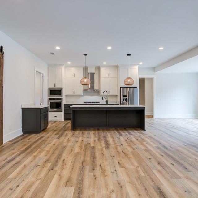 Room with white walls and wooden floors and open concept kitchen - Rafter B Construction custom home