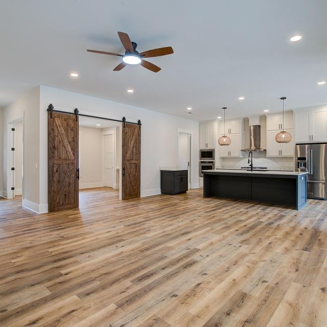 Room with white walls and wooden floors and open concept kitchen - Rafter B Construction custom home