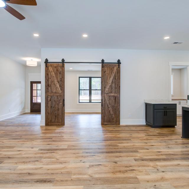 Room with white walls and wooden floors and open concept kitchen - Rafter B Construction custom home